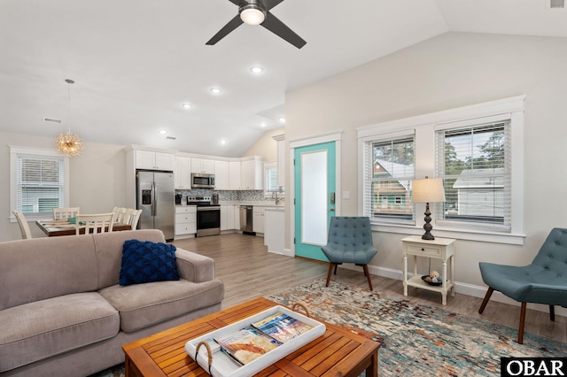 living room with vaulted ceiling, ceiling fan with notable chandelier, baseboards, and light wood-style floors