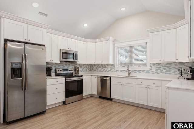 kitchen with visible vents, white cabinets, vaulted ceiling, stainless steel appliances, and a sink