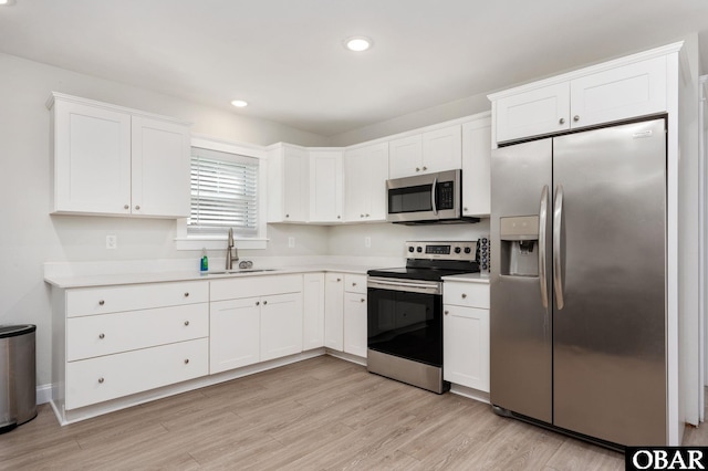 kitchen featuring stainless steel appliances, light countertops, light wood-style floors, white cabinetry, and a sink