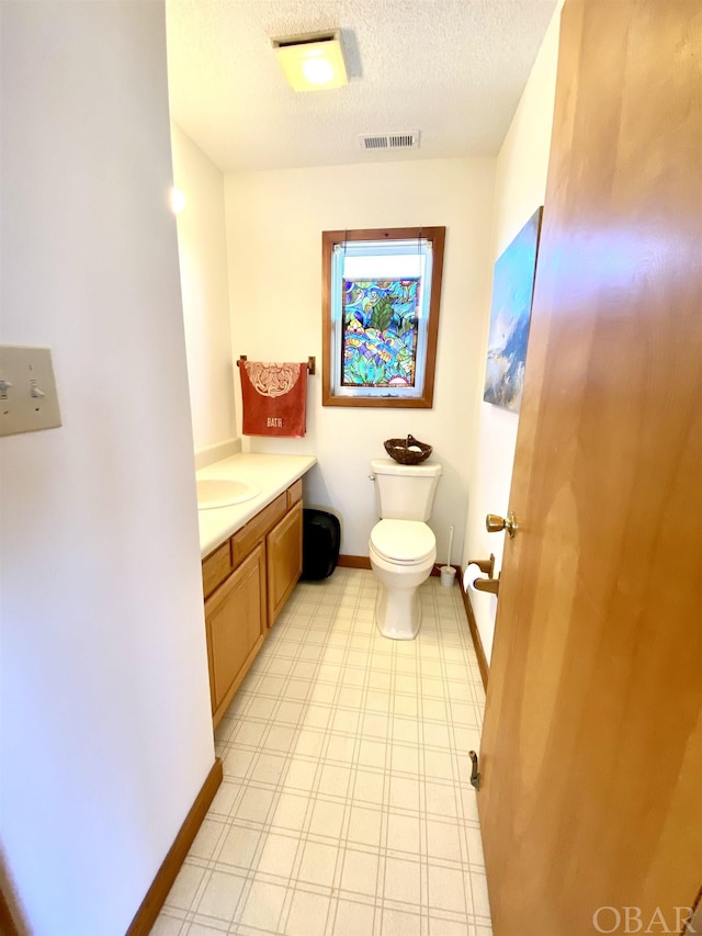 bathroom with baseboards, visible vents, toilet, a textured ceiling, and vanity