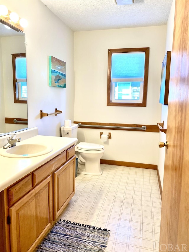 bathroom featuring a textured ceiling, vanity, toilet, and baseboards