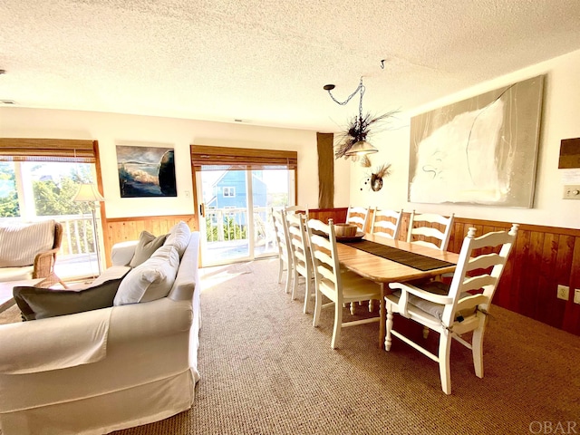 carpeted dining area featuring a textured ceiling, wood walls, and wainscoting