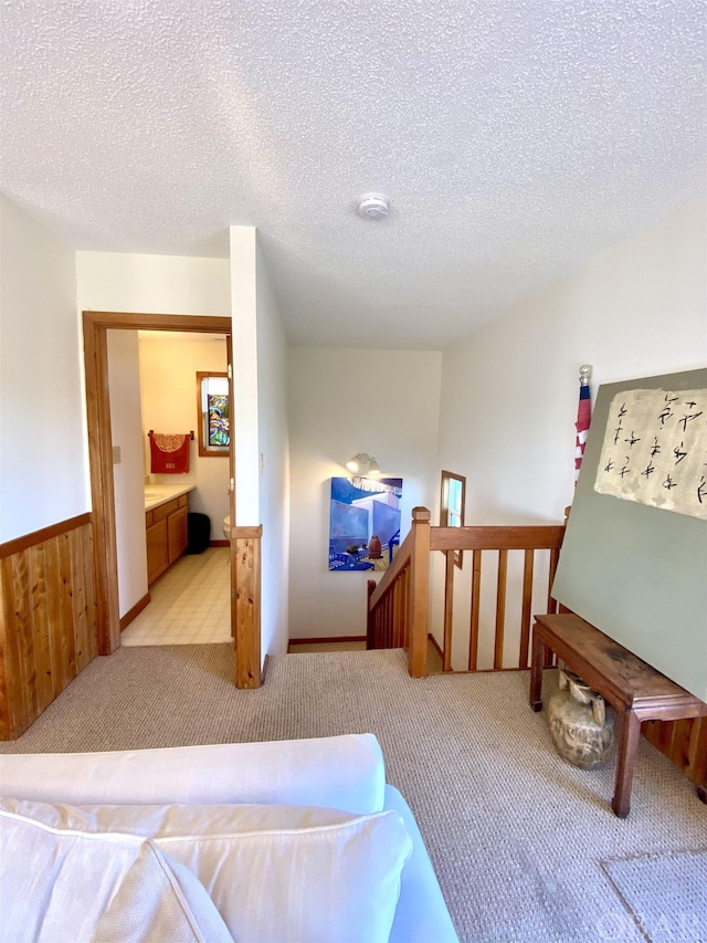 interior space featuring light carpet, a wainscoted wall, a textured ceiling, and an upstairs landing