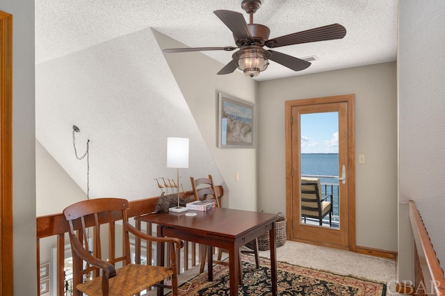 office area with a textured ceiling, carpet floors, a water view, visible vents, and a ceiling fan