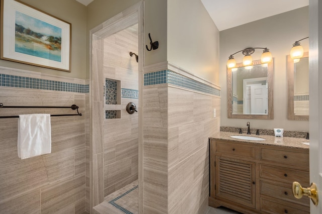 bathroom featuring tile walls, a tile shower, vanity, and a wainscoted wall