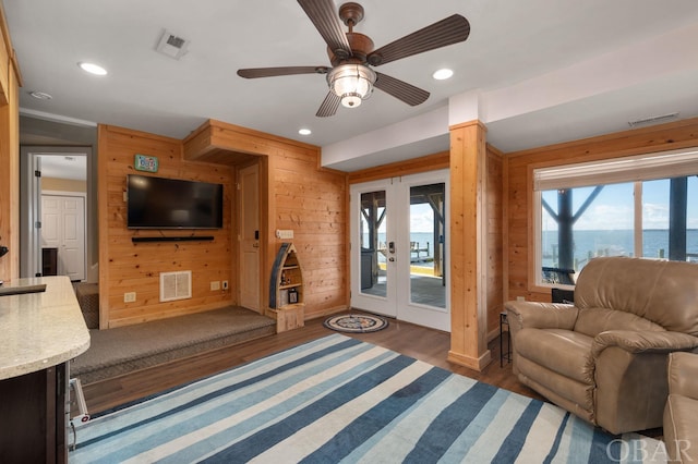 living area featuring dark wood-type flooring, a water view, visible vents, and wooden walls