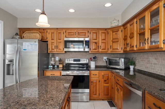 kitchen featuring tasteful backsplash, appliances with stainless steel finishes, brown cabinets, dark stone counters, and a toaster