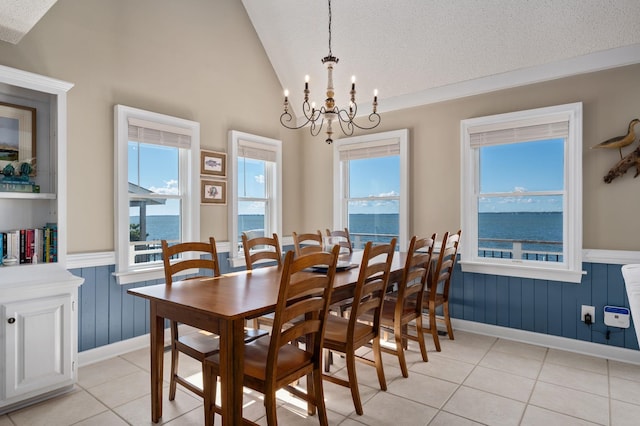 dining space with light tile patterned floors, wainscoting, a notable chandelier, and vaulted ceiling