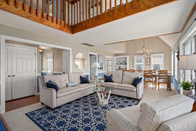 living room with light tile patterned floors, visible vents, a chandelier, and high vaulted ceiling