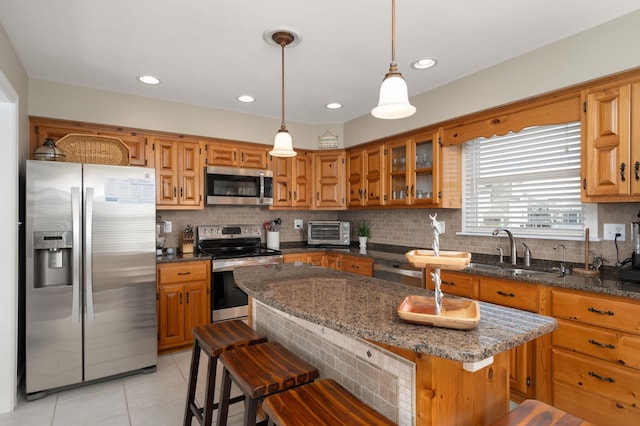 kitchen with light tile patterned floors, tasteful backsplash, a sink, stainless steel appliances, and brown cabinets