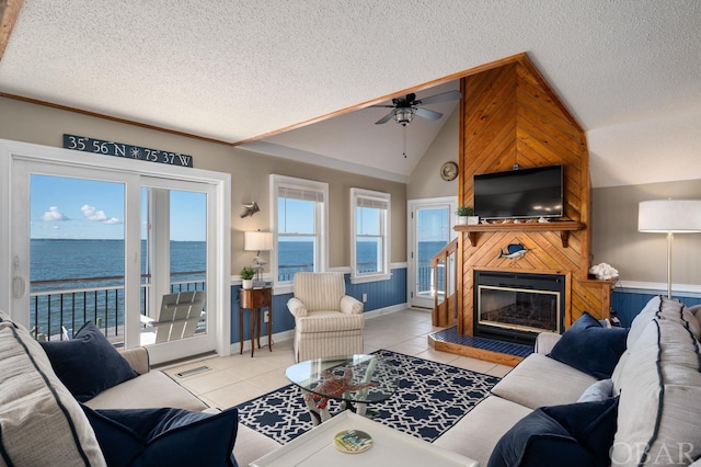 living area featuring a fireplace, light tile patterned floors, a water view, vaulted ceiling, and a textured ceiling