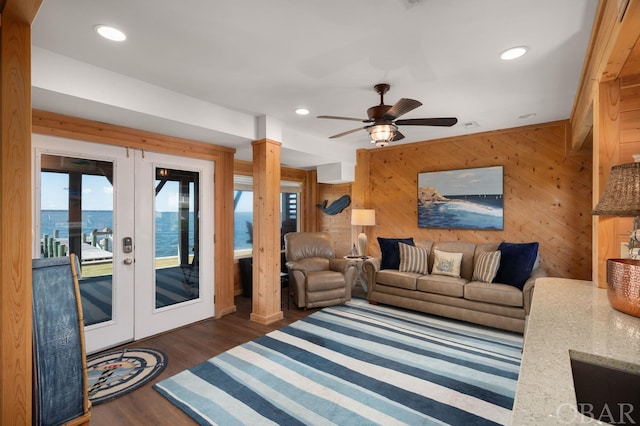 living area featuring french doors, dark wood finished floors, recessed lighting, a water view, and wooden walls