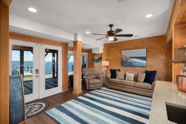 living room with a ceiling fan, french doors, wooden walls, and dark wood finished floors