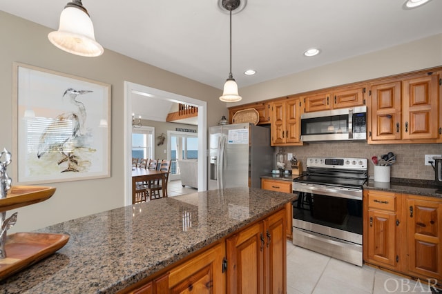 kitchen featuring decorative light fixtures, decorative backsplash, appliances with stainless steel finishes, brown cabinetry, and dark stone countertops