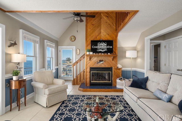 living area with light tile patterned floors, a water view, a ceiling fan, a large fireplace, and vaulted ceiling