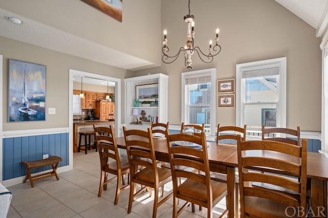 dining room featuring light tile patterned floors, high vaulted ceiling, a notable chandelier, and wainscoting