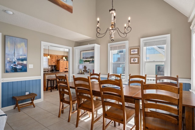 dining space featuring high vaulted ceiling, light tile patterned floors, wainscoting, and an inviting chandelier