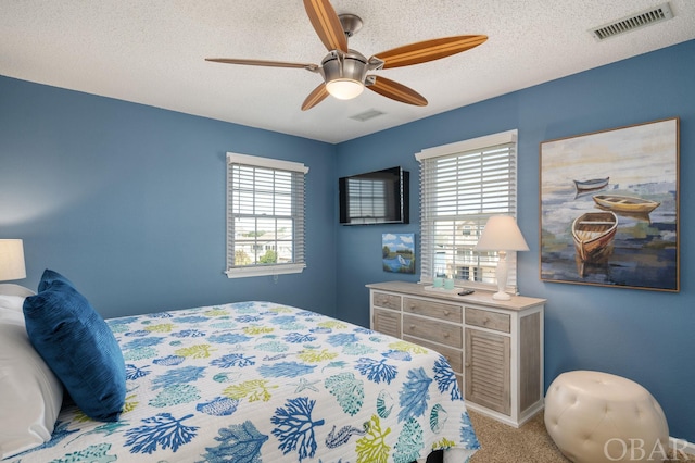 bedroom with light carpet, a ceiling fan, visible vents, and a textured ceiling