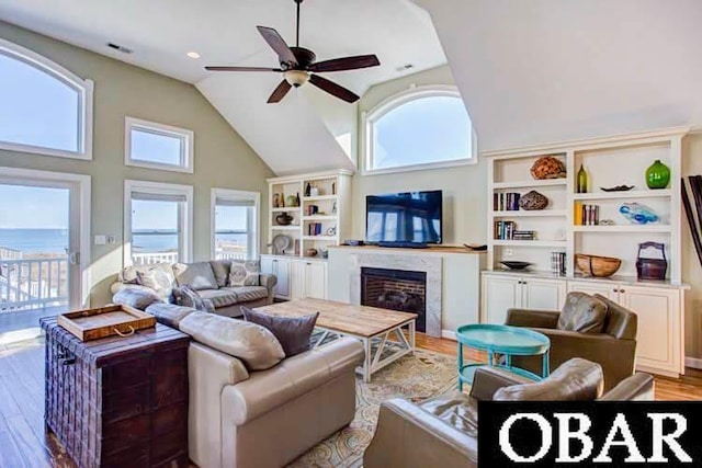 living room with visible vents, light wood-style floors, a high end fireplace, ceiling fan, and high vaulted ceiling