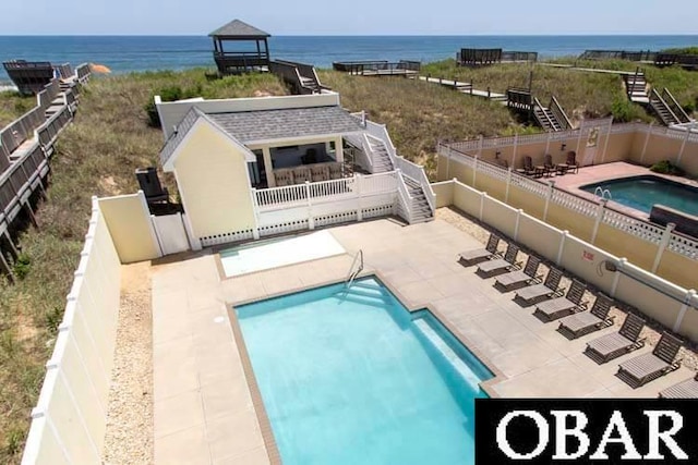 community pool with a patio area, a fenced backyard, a water view, and stairs