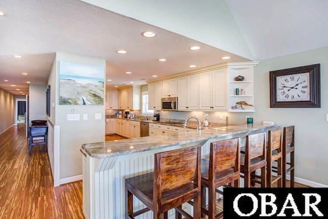 kitchen featuring light stone counters, a peninsula, wood finished floors, a kitchen breakfast bar, and appliances with stainless steel finishes