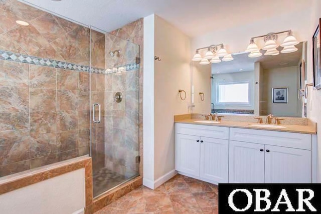 full bathroom featuring double vanity, a shower stall, baseboards, and a sink