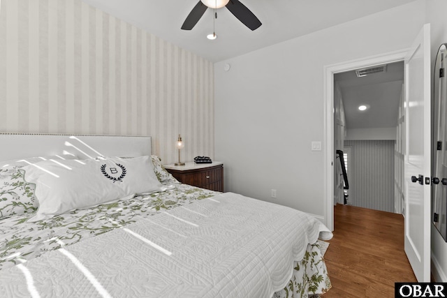 bedroom featuring wood finished floors, a ceiling fan, baseboards, visible vents, and wallpapered walls