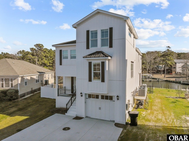 view of front of house with concrete driveway, a water view, an attached garage, a standing seam roof, and a front lawn