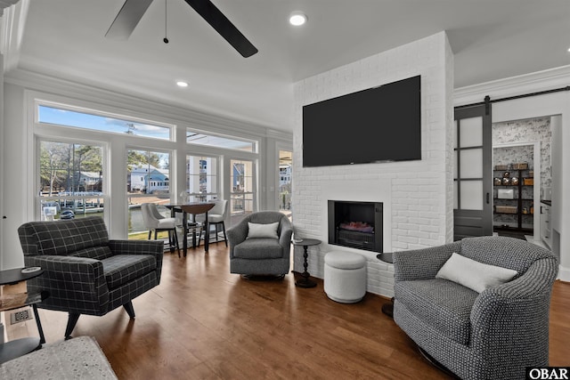 living area featuring a barn door, a ceiling fan, ornamental molding, wood finished floors, and a brick fireplace