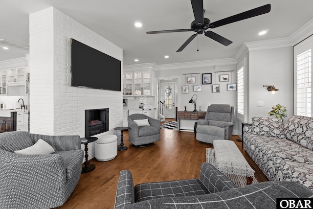 living area featuring recessed lighting, ornamental molding, a ceiling fan, a brick fireplace, and wood finished floors