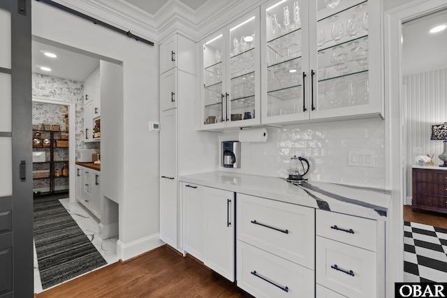 bar with marble finish floor, backsplash, a barn door, ornamental molding, and baseboards