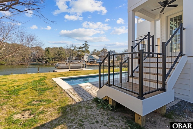 view of pool with a yard, a dock, a water view, and a ceiling fan