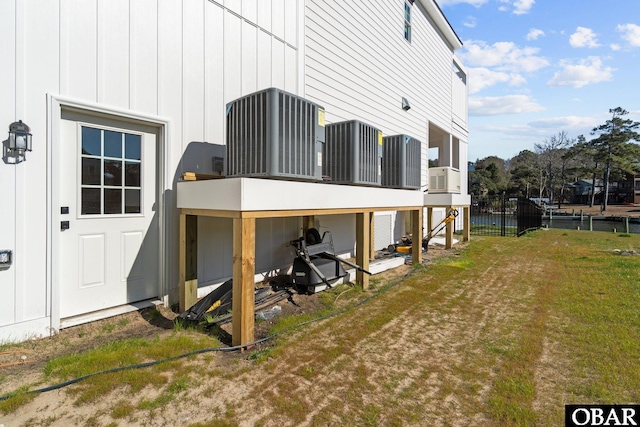 back of property with a lawn, central AC unit, and board and batten siding