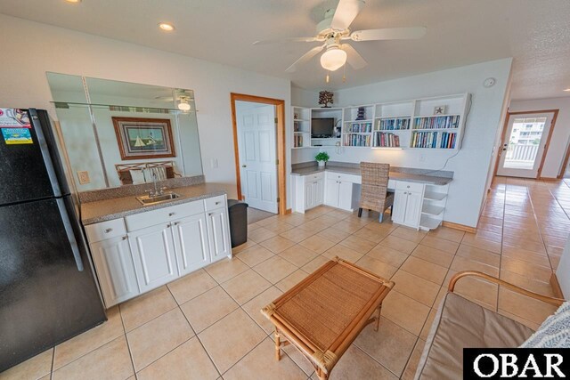 kitchen with a sink, light tile patterned floors, built in study area, white cabinets, and freestanding refrigerator
