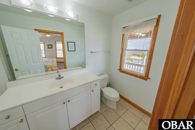 ensuite bathroom with connected bathroom, ceiling fan, toilet, tile patterned floors, and vanity