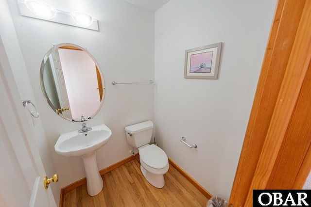 half bathroom featuring baseboards, wood finished floors, toilet, and a sink