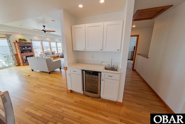kitchen with light wood finished floors, a sink, wine cooler, visible vents, and white cabinetry