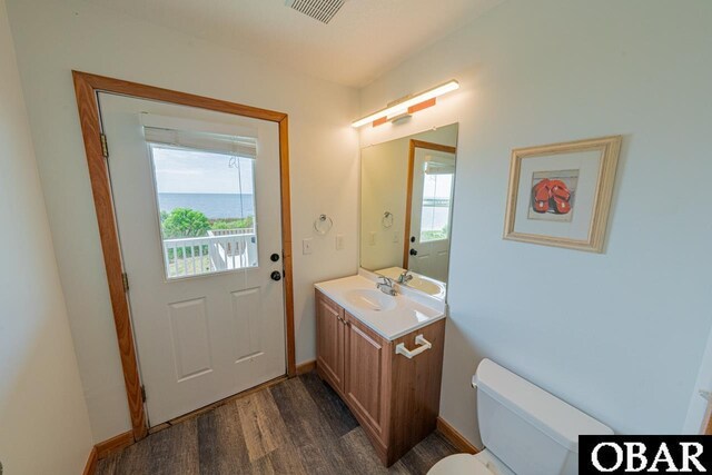 half bath with visible vents, wood finished floors, toilet, and plenty of natural light