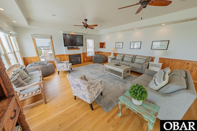 living area with a wealth of natural light, wainscoting, a raised ceiling, and ceiling fan