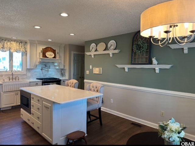 kitchen with light countertops, a kitchen island, white cabinetry, and built in microwave