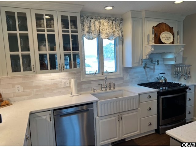 kitchen with stainless steel appliances, a sink, white cabinetry, light countertops, and glass insert cabinets