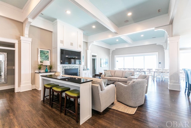 living area with ornate columns, a tiled fireplace, dark wood-style floors, and beam ceiling