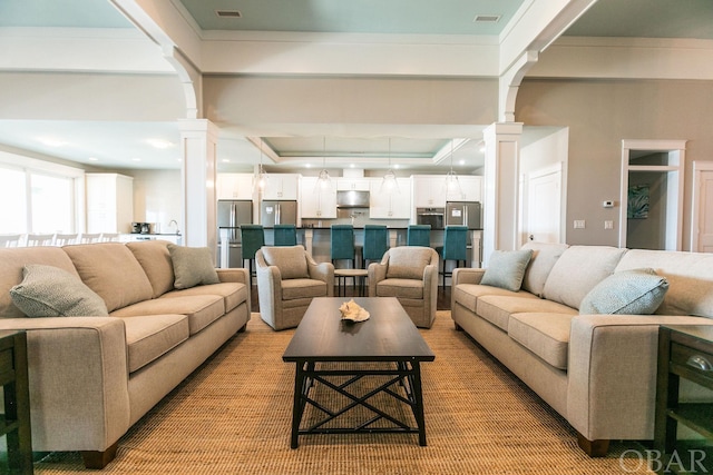 living area featuring arched walkways, visible vents, a raised ceiling, and decorative columns