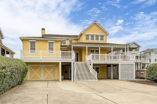 beach home featuring an attached garage, covered porch, stairs, driveway, and a chimney