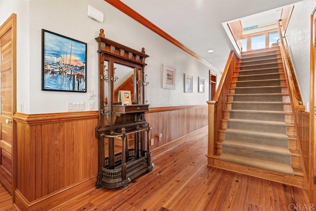 staircase with wainscoting, ornamental molding, wood finished floors, wood walls, and recessed lighting