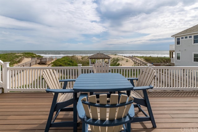 wooden terrace featuring outdoor dining space, a water view, a beach view, and a gazebo