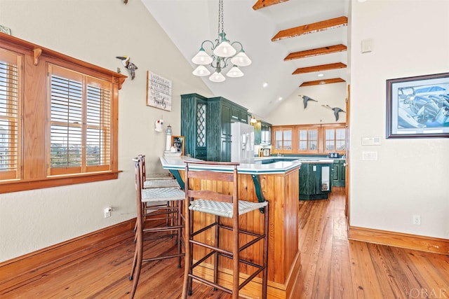 kitchen featuring a breakfast bar area, a peninsula, green cabinetry, white fridge with ice dispenser, and pendant lighting