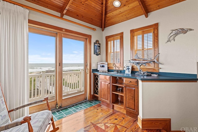 bar featuring vaulted ceiling with beams, a beach view, a water view, a sink, and wooden ceiling