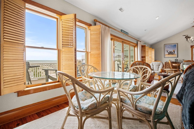 dining area featuring baseboards, visible vents, lofted ceiling, wood finished floors, and a water view