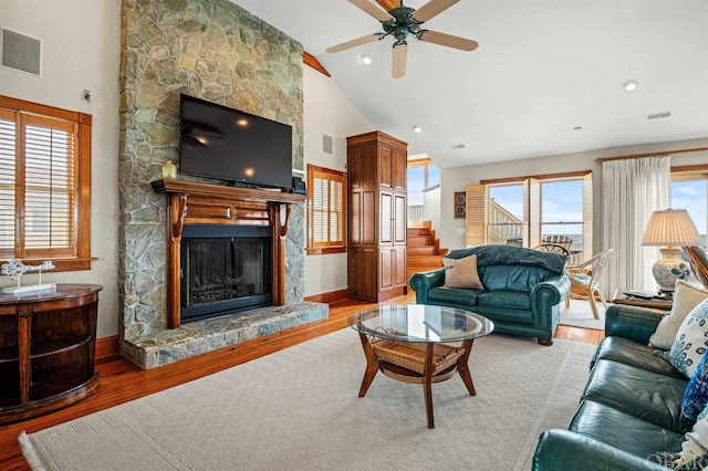 living area featuring visible vents, a stone fireplace, wood finished floors, high vaulted ceiling, and baseboards